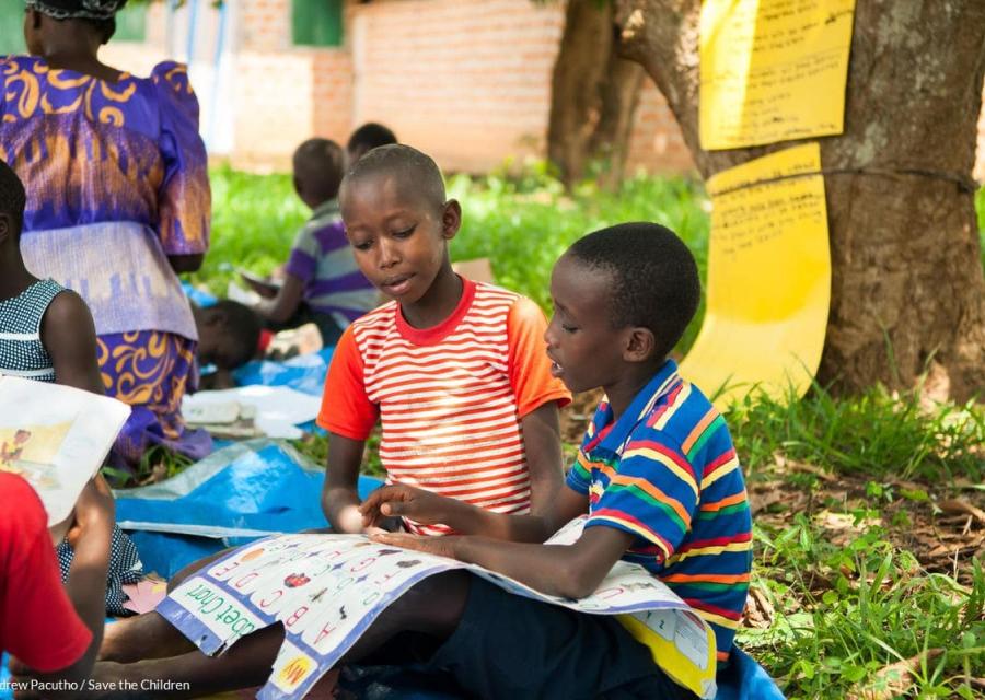 bambini seduti su un prato che leggono un cartellone con i numeri 
