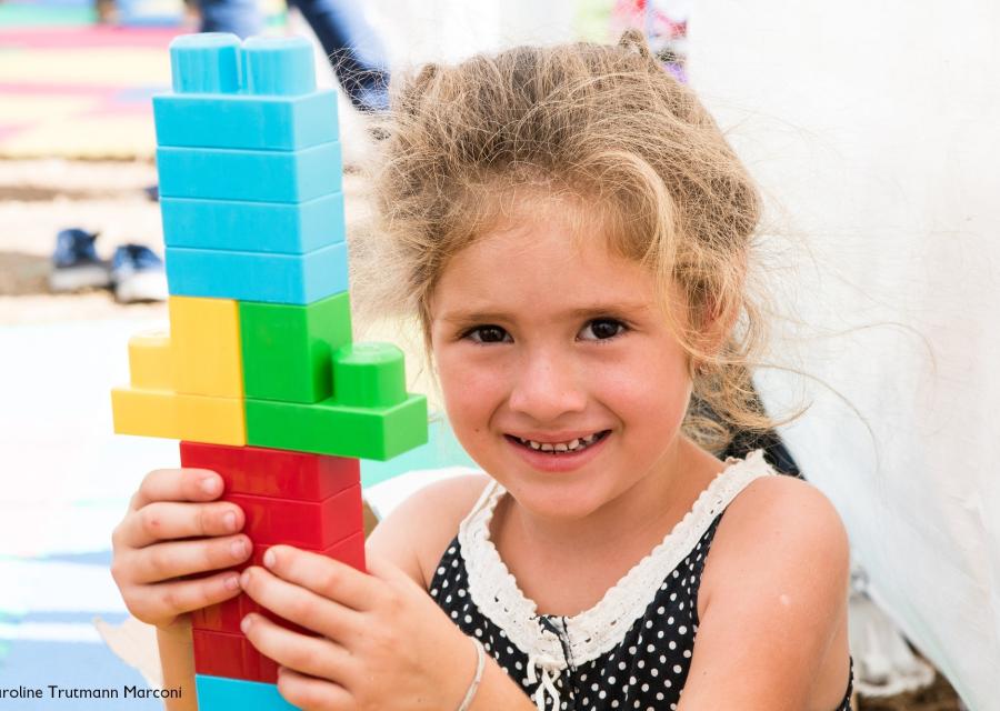 bambina sorridente con in mano una costruzione fatta di Lego colorati