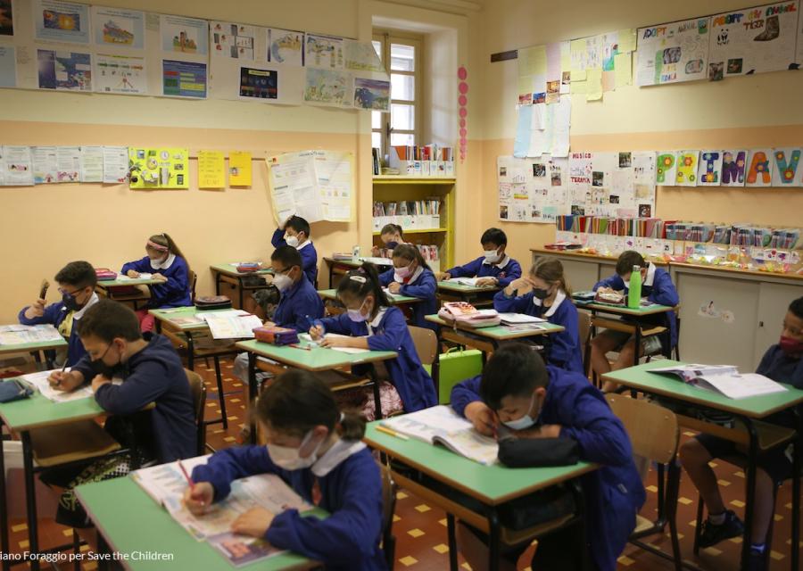 bambine e bambini sui banchi di scuola che scrivono su un foglio 