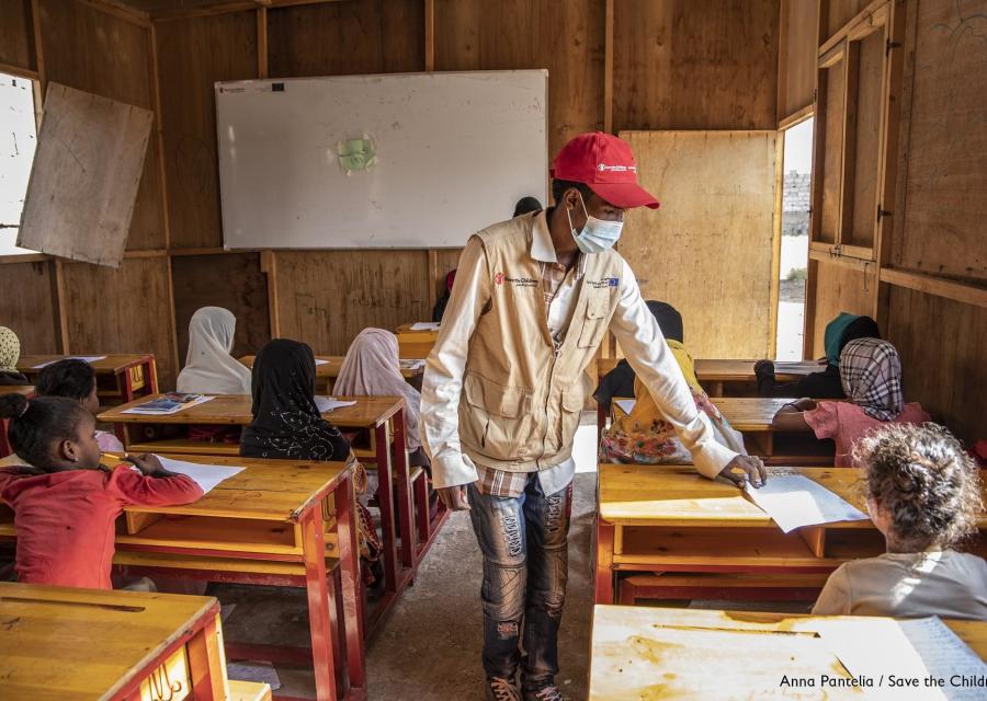 Un operatore save the children in piedi tra i banchi dei bambini in un aula scolastica di un campo rifugiati in Yemen