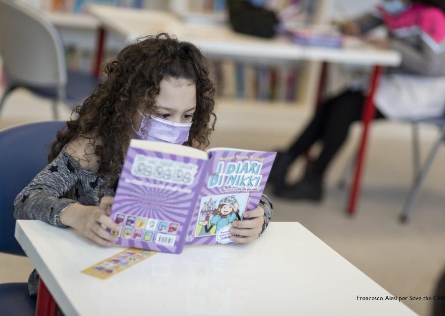 bambina mora con capelli ricci lunghi legge un libro seduta a una scrivania