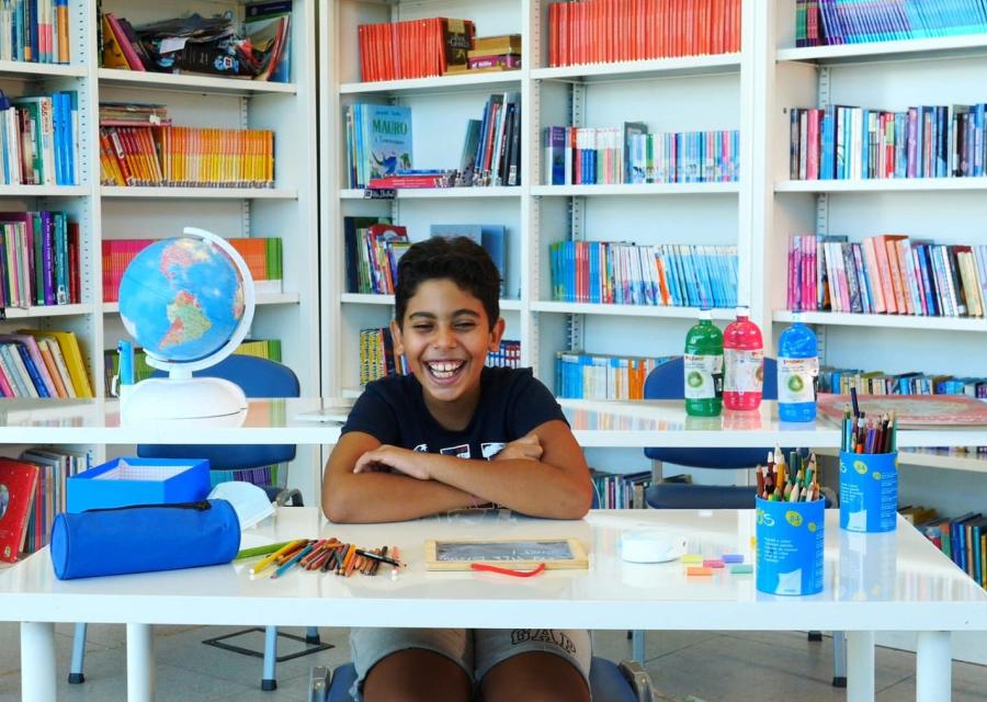 bambino seduto a scrivania con libri e penne sorride