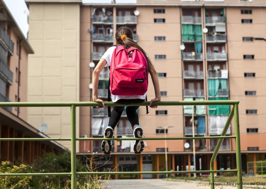 bambina seduta su una ringhiera verde davanti a dei palazzi