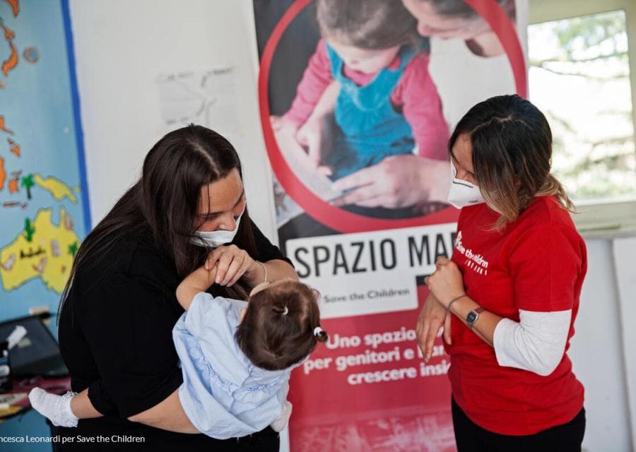bambina in braccio alla madre mentre scherza con operatrice di save the children all interno dei nostri spazi mamme