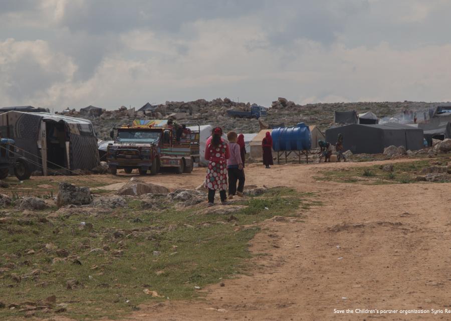 bambini di spalle in lontananza sullo sfondo di un accampamento di fortuna nel nord ovest della Siria