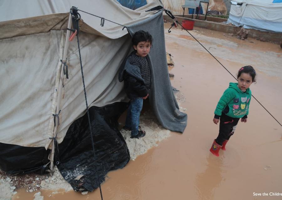 Due bambini siriani fuori alla loro tenda in un campo profughi stanno in piedi nel terreno allagato