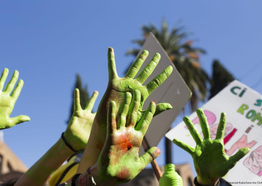 Mani verdi di bambini alzate al cielo con cartelloni