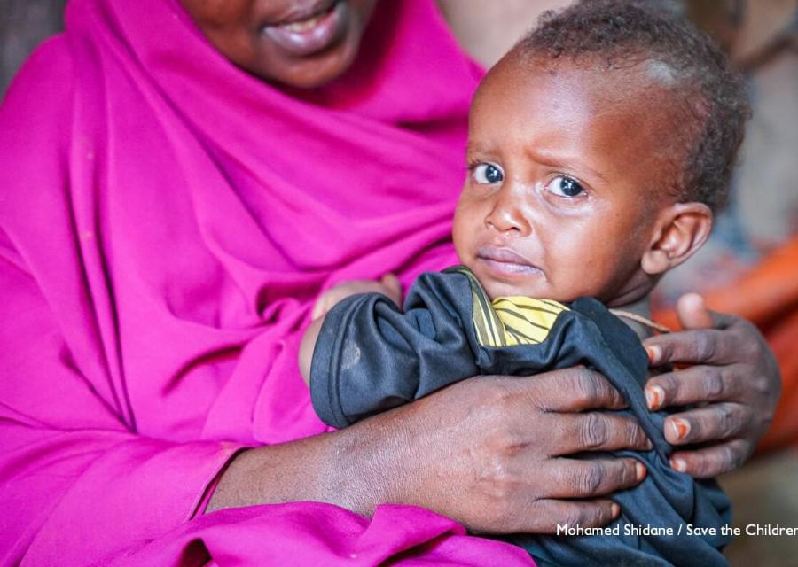 bambino somalo con sguardo triste in braccio a donna con veste fucsia