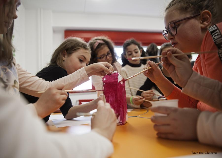5 ragazze al banco di scuola stanno dipingendo di rosa un loro lavoro artistico