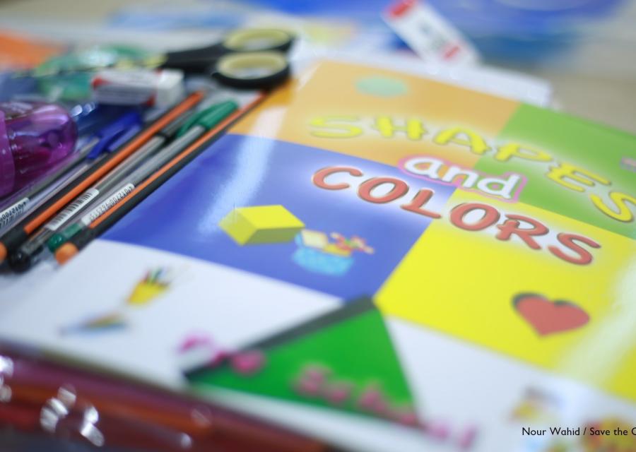 dettaglio di un banco di scuola con un libro colorato con a fianco matite, penne e altri strumenti per il disegno