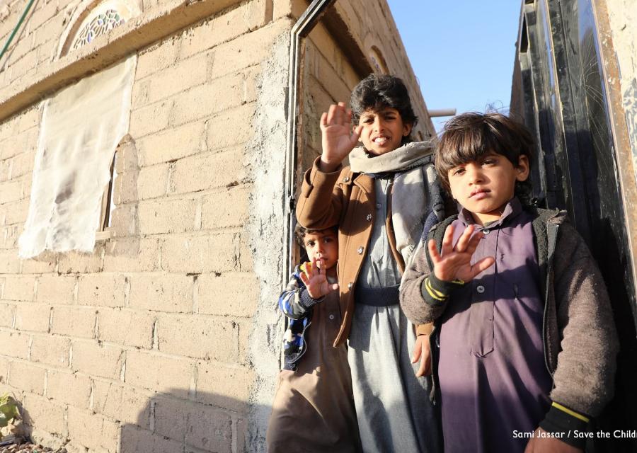 Tre bambini  yemeniti in piedi tra due edifici mostrano la mano aperta a cinque