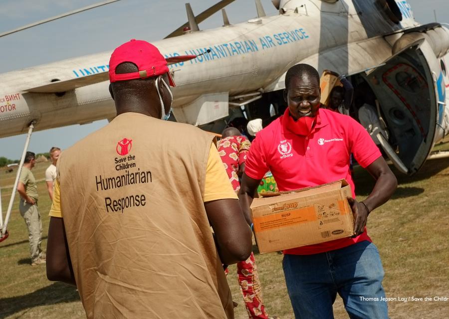Operatori save the children trasportano in mano scatole di aiuti umanitari appena arrivati da un aereo. Un operatore è di spalle e l altro è di fronte.