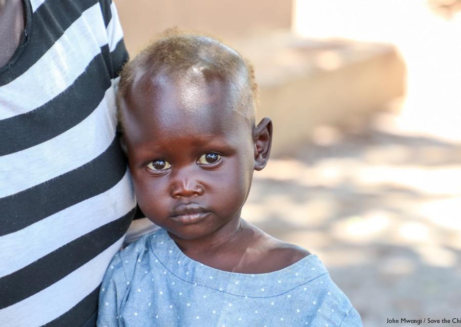 primo piano di un bambino sud sudanese con maglietta grigia è vicino alla pancia di un adulto con maglietta a righe bianche e nere