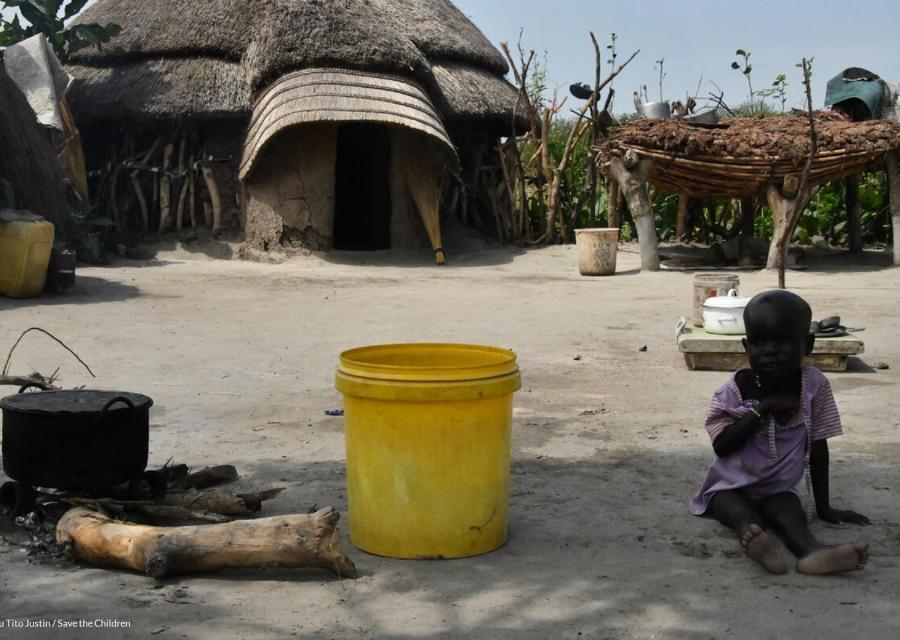 bambino seduto a terra accanto secchio giallo acqua