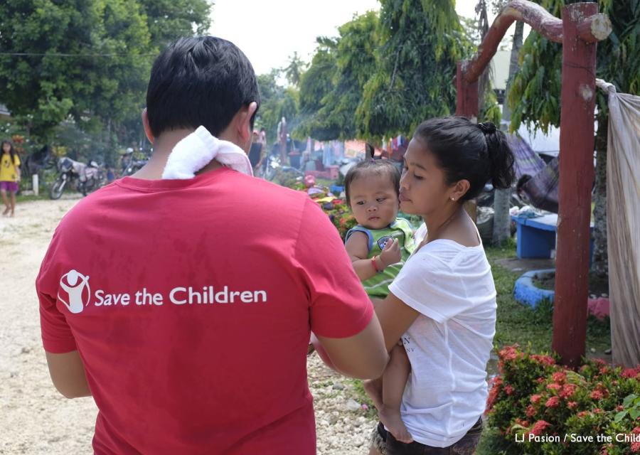 Operatore Save the Children presta assistenza a una mamma filippina con bambino in braccio
