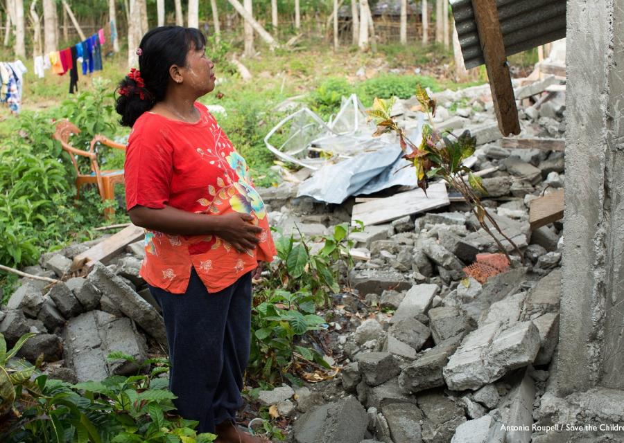 Donna indonesiana in cinta sta in piedi di profilo e guarda di fronte a lei un abitazione distrutta dal terremoto