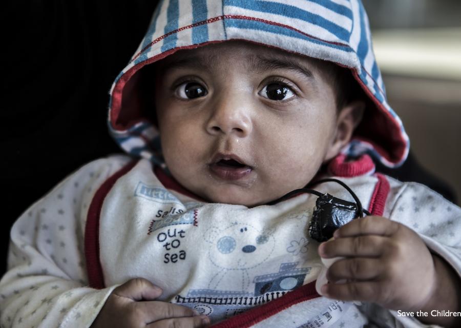 bambino di pochi mesi inquadrato in primo piano con tutina e cappuccio sulla testa