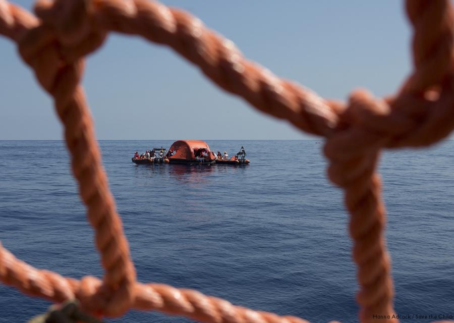 primo piano di una rete rossa di una barca dalla quale si vede il mare e un barchino di salvataggio a pochi metri