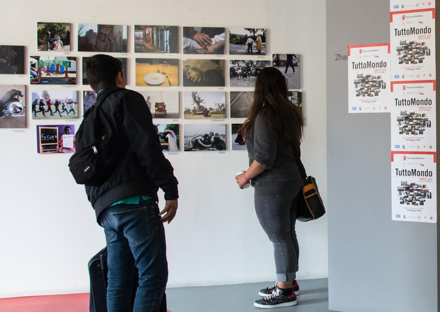 due ragazzi in un museo, in piedi, di spalle, guardano delle fotografie appese a un muro