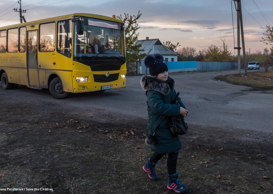 bambina cammina di fronte ad uno scuola bus giallo in Ucraina