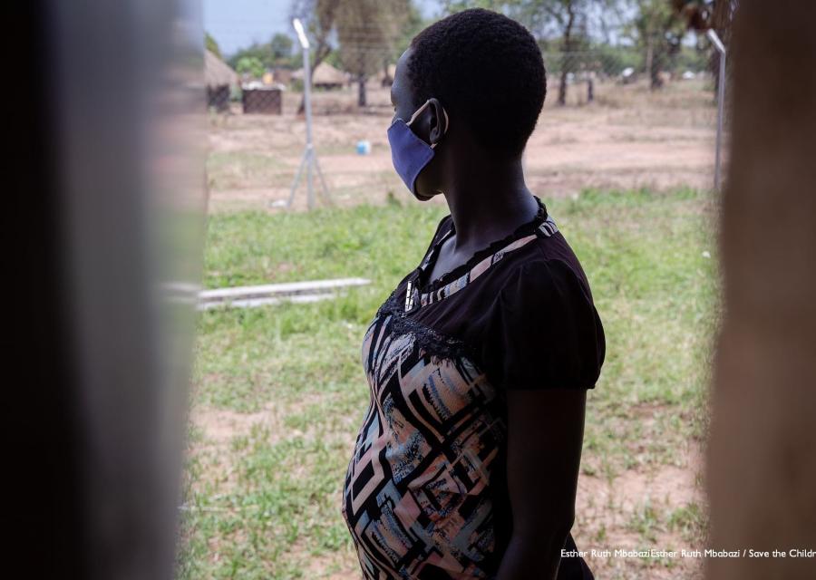 una ragazza ugandese vista attraverso una finestra è girata dall altro lato e guarda un prato verde. La ragazza è incinta e indossa una maglietta nera con motivi floreali.