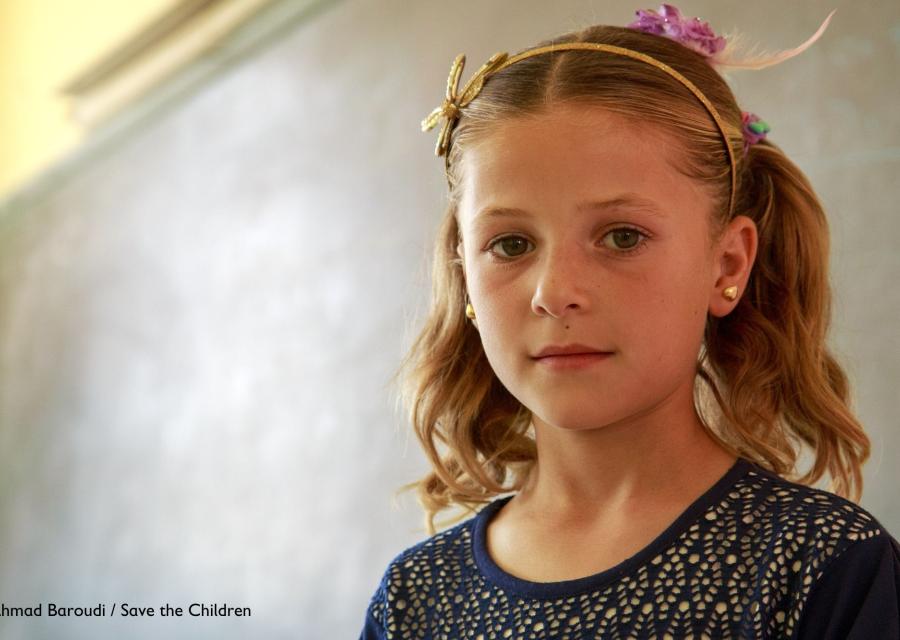 Bambina bianca bionda con i codini e un cerchietto rosa sui capelli sta davanti a una lavagna a scuola