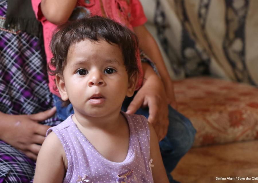Bambino di 13 mesi con una canottiera rosa è tenuto per le spalle da una donna che non si vede in faccia.
