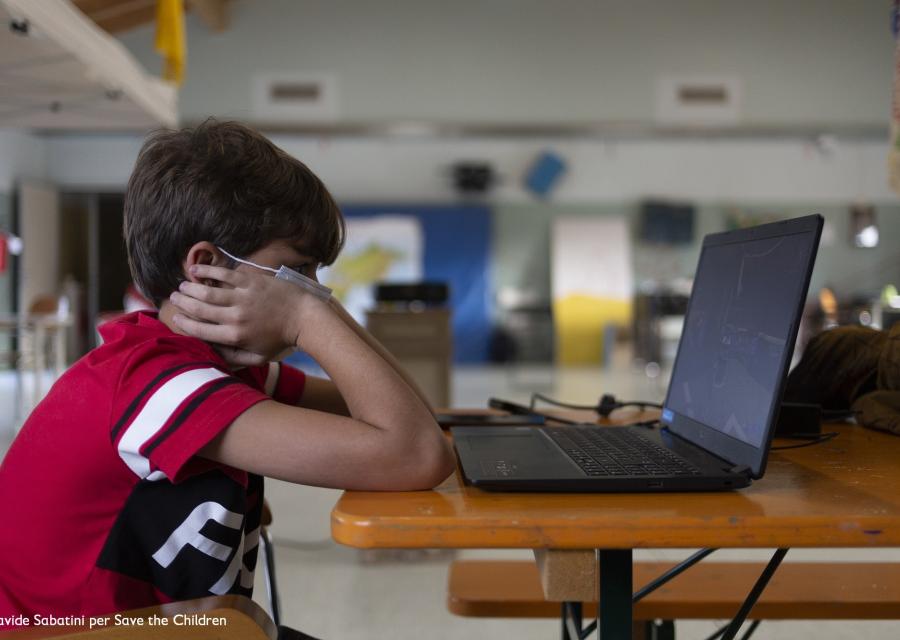 bambino seduto davanti al PC indossa una mascherina per proteggersi dal covid-19
