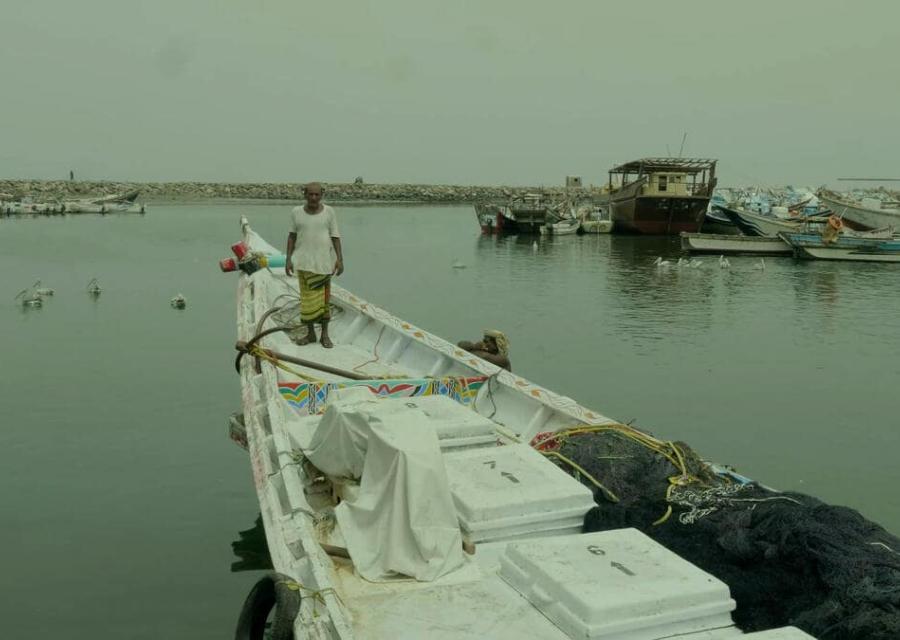 pescatore con maglia bianca in piedi sulla prua di una barca bianca ormeggiata al porto in Yemen