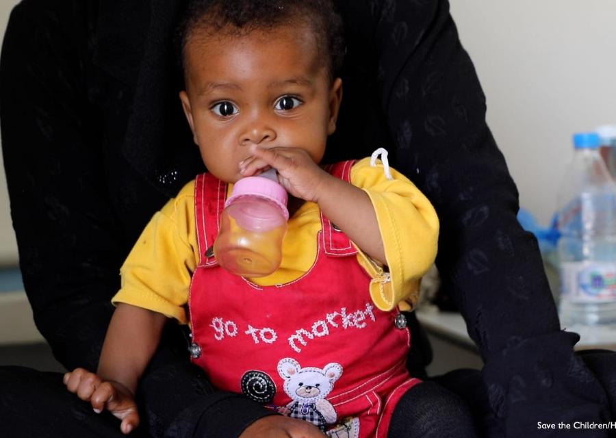 Bambino yemenita con biberon in bocca in braccio alla madre.