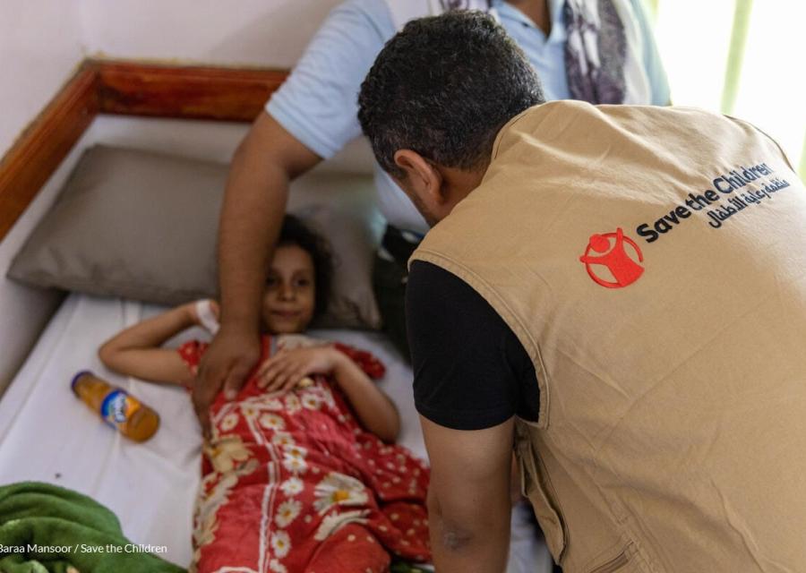 bambina colpita da un bombardamento in yemen su un letto di una nostra clinica con accanto un operatore save the children