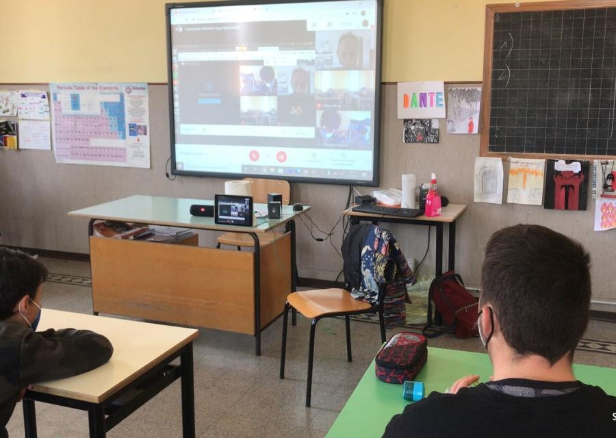 Classe con due ragazzi di spalle seduti al banchi che guardano uno schermo che proietta teams