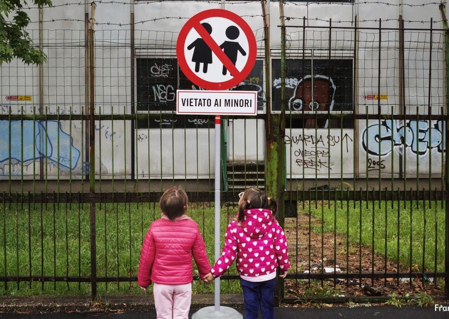 due bambine si tengono per mano davanti a un cartello di divieto con scritto "vietato ai minori"