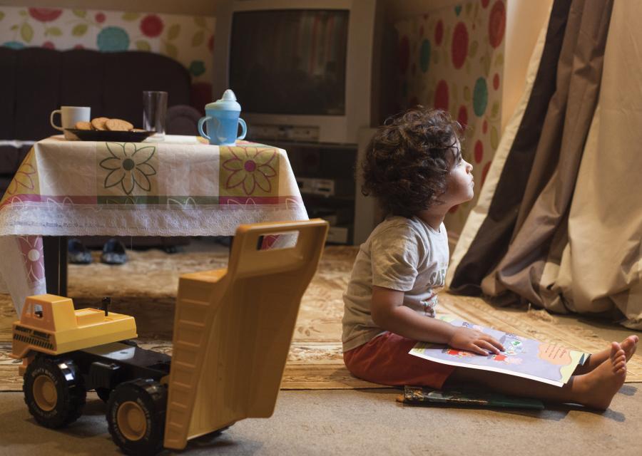 Bambino seduto a terra con libro sulle gambe guarda fuori dalla finestra