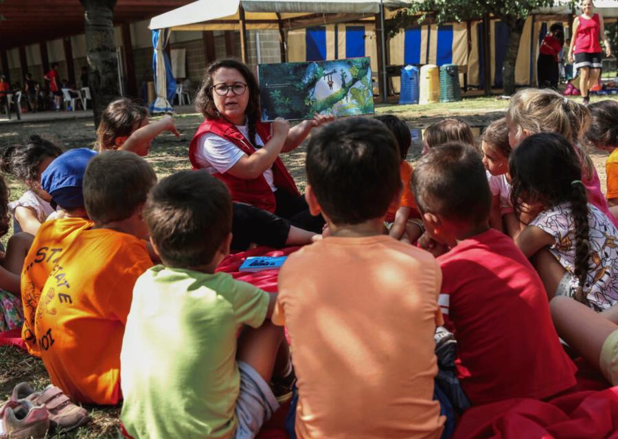 bambini in cerchio di spalle che ascoltano un'operatrice 