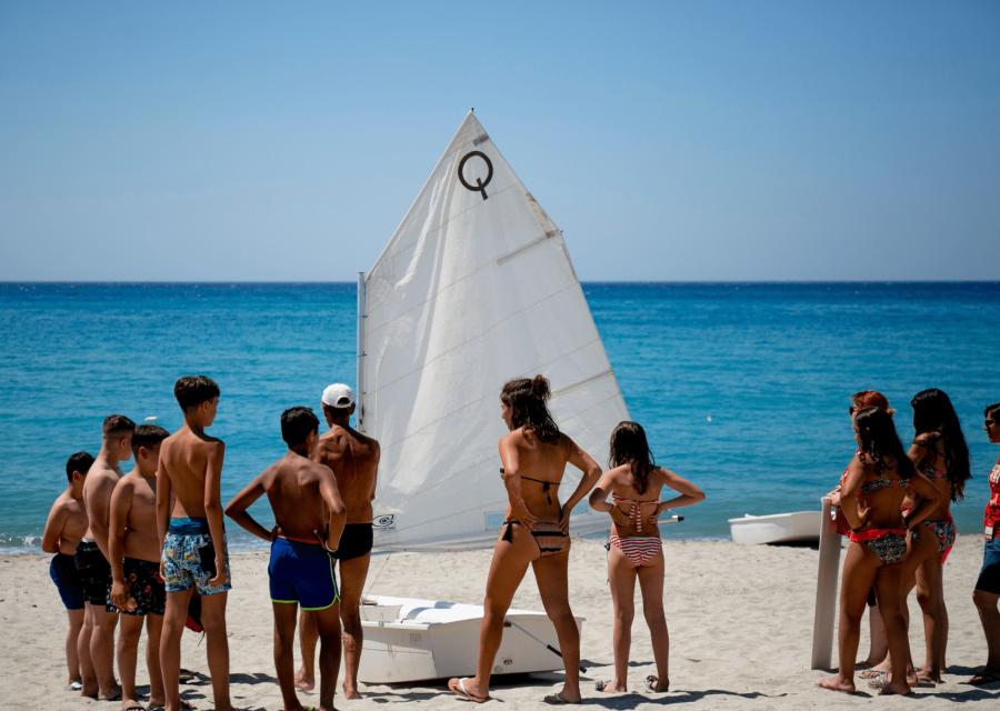 Bambini e bambine su una spiaggia davanti ad una barchetta a vela