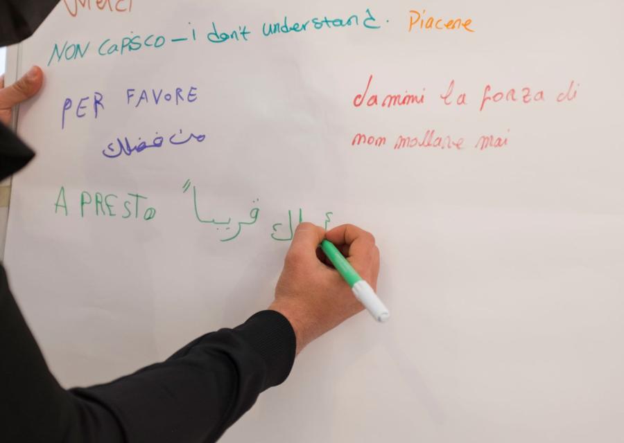 Ragazzo scrive, su un cartellone pieno di frasi scritte in diverse lingue, un messaggio in arabo.