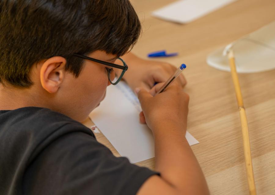 bambino con occhiali scrive parole su un foglio a scuola 