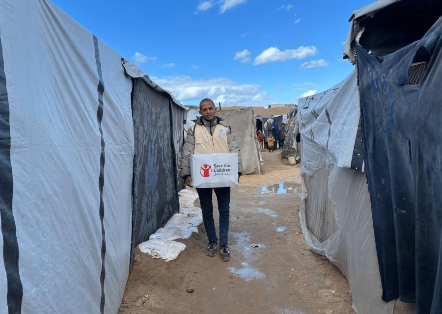 Operatore umanitario Save the Children a Gaza con pacco in mano tra le tende