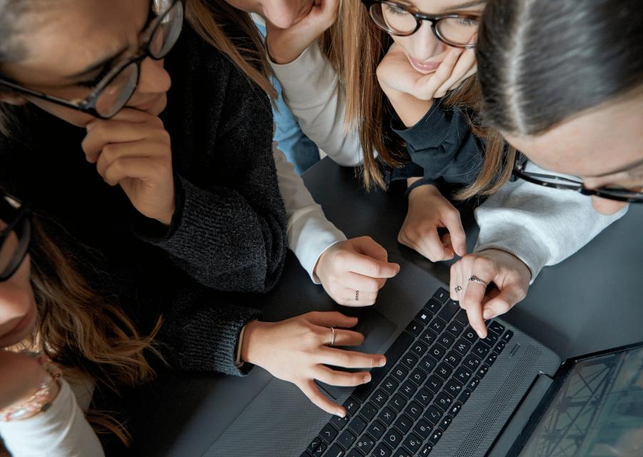 Quattro ragazze intorno a un computer che guardano lo schermo e toccano la tastiera.
