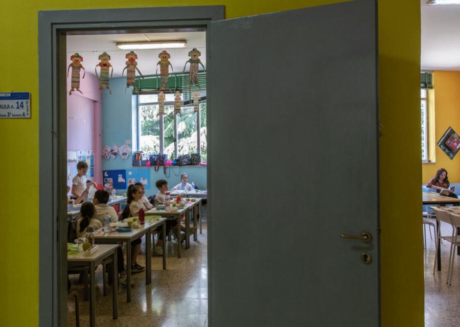 porta di aula scolastica con dentro bambini e bambine seduti tra i banchi