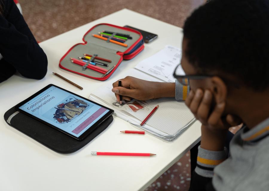 bambino che scrive su libro con altri materiali scolastici sul banco 