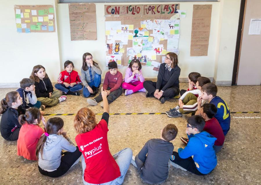 Bambini seduti per terra, in cerchio, durante il consiglio Fuoriclasse, con operatrice Save The Children e insegnante.