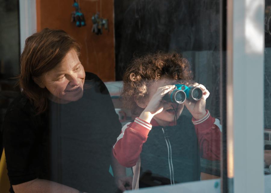 Bambino con binocolo che guarda fuori dalla finestra con adulta che lo affianca