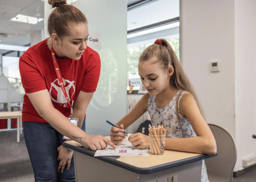 operatrice aiuta una bambina seduta su una scrivania a colorare un disegno
