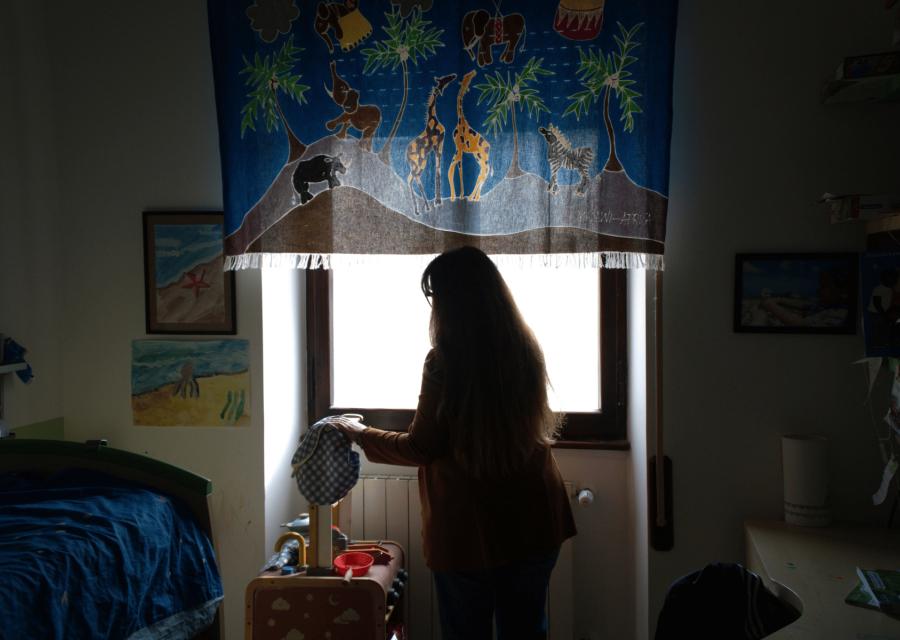 Donna di spalle in controluce davanti ad una finestra nella stanza del figlio 