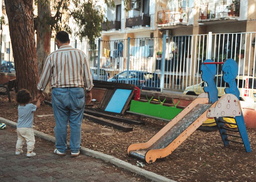 Papà di spalle mano nella mano con figlia piccola in un parco giochi 