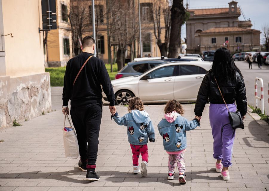 Una mamma e un papà che camminano accompagnando per mano le due figlie gemelle tutti di schiena
