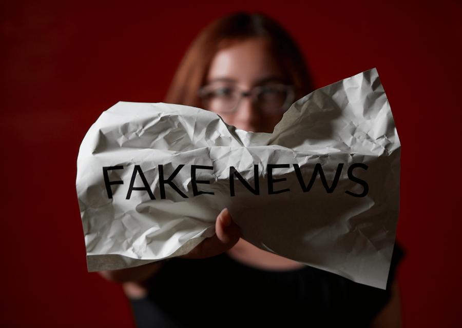 Ragazza in secondo piano che stringe un foglio con scritto Fake News