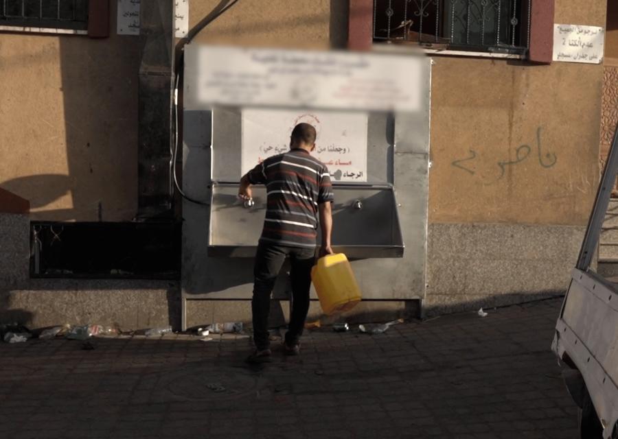 Uomo che prova ad usare un rubinetto rotto per mettere dell'acqua in un serbatoio giallo